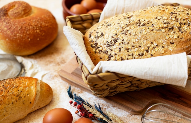 Concetto di panetteria. Un assortimento di diversi tipi di pane su uno sfondo di marmo chiaro. Uova, farina, spighe di grano. Avvicinamento