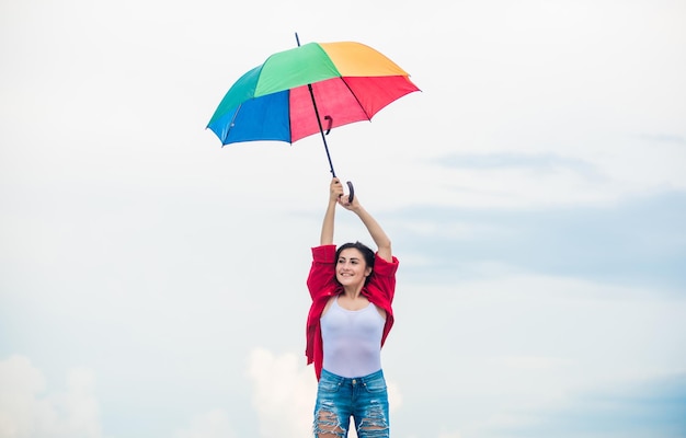 Concetto di paracadute Persona di mentalità aperta Ragazza che si sente bene sullo sfondo del cielo Bel tempo Autunno accogliente Bella donna con ombrello colorato Ombrello arcobaleno Tempo piovoso Buon umore Buone vibrazioni