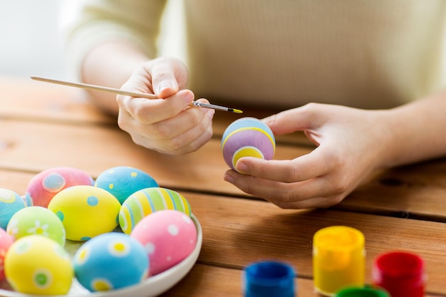 concetto di pasqua, vacanze, tradizione e persone - primo piano delle mani della donna che colorano le uova di pasqua con colori e pennello