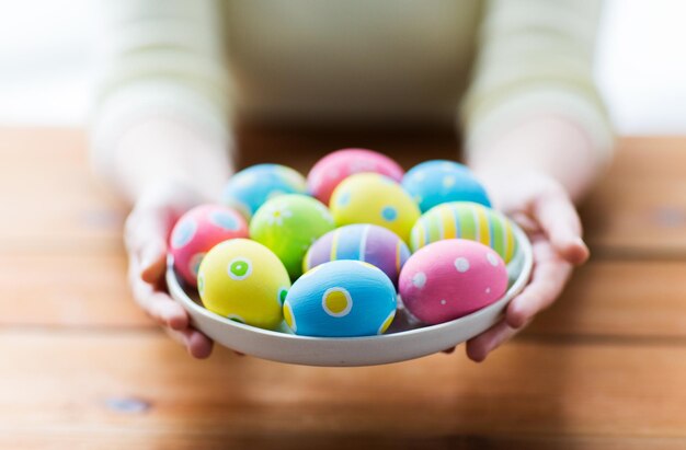 concetto di pasqua, vacanze, tradizione e persone - primo piano delle mani della donna che tengono le uova di pasqua colorate sul piatto