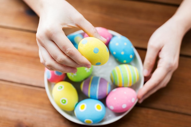 concetto di pasqua, vacanze, tradizione e persone - primo piano delle mani della donna con uova di pasqua colorate sul piatto