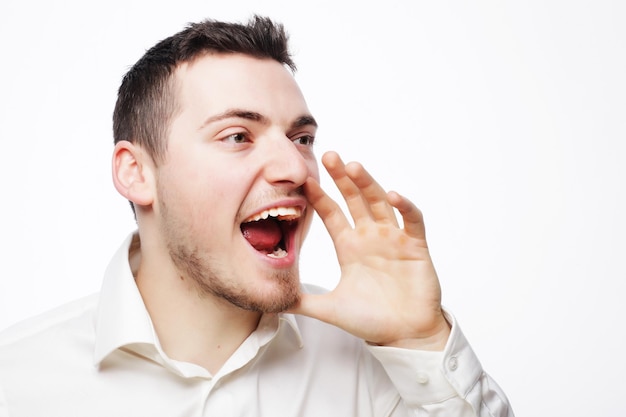 Concetto di persone, affari e stile di vita - bell'uomo d'affari in camicia bianca che grida mentre guarda la telecamera e sta in piedi su sfondo bianco