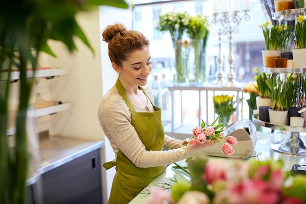 concetto di persone, affari, vendita e floristica - donna fiorista sorridente felice che fa mazzo di tulipani al negozio di fiori