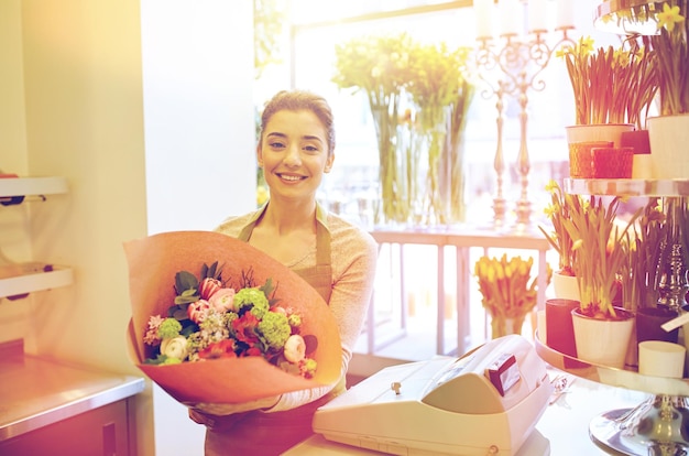 concetto di persone, affari, vendita e floristica - donna fiorista sorridente felice che tiene mazzo di fiori avvolto in carta al negozio di fiori