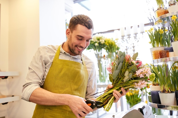 concetto di persone, affari, vendita e floristica - felice fiorista sorridente che fa un mazzo e taglia steli con le forbici al negozio di fiori