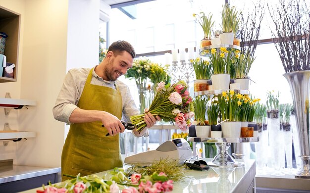 concetto di persone, affari, vendita e floristica - felice fiorista sorridente che fa un mazzo e taglia steli con le forbici al negozio di fiori