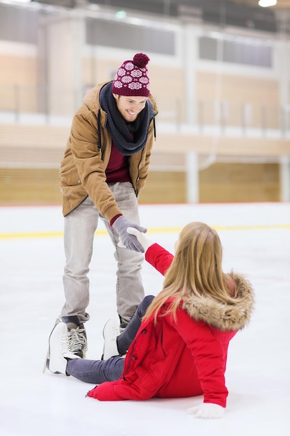 concetto di persone, amicizia, sport e tempo libero - uomo sorridente che aiuta le donne a salire sulla pista di pattinaggio