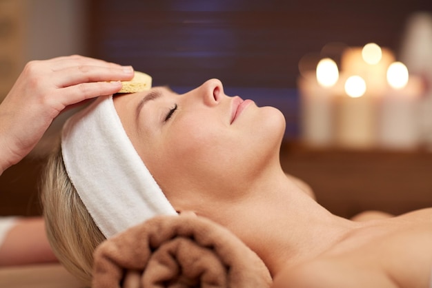 concetto di persone, bellezza, spa, cosmetologia e relax - primo piano di bella giovane donna sdraiata con gli occhi chiusi con pulizia del viso con spugna nella spa