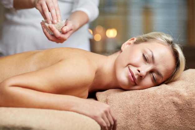 concetto di persone, bellezza, spa, massaggi e relax - primo piano di bella giovane donna sdraiata con gli occhi chiusi e terapista che tiene una ciotola di sale nella spa