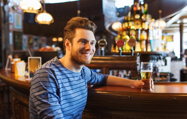 concetto di persone, bevande, alcol e tempo libero - giovane felice che beve birra al bar o al pub
