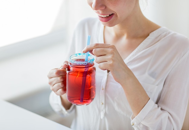 concetto di persone, bevande e vacanze - primo piano di una donna felice che beve succo da una tazza di vetro con paglia a casa