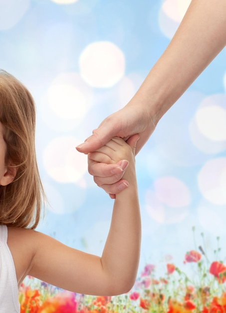 concetto di persone, carità, famiglia e adozione - primo piano di donna e bambina che si tengono per mano su luci blu e sfondo del campo di papaveri