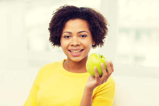 concetto di persone, cibo, alimentazione sana e cure odontoiatriche - felice giovane donna afroamericana con mela verde a casa