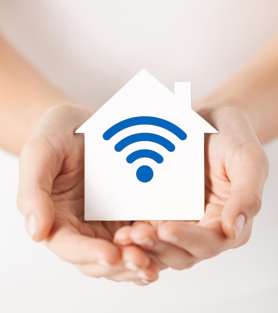 concetto di persone, connessione internet, sicurezza, allarme e tecnologia - primo piano delle mani che tengono la casa con l'icona del segnale dell'onda radio o wifi