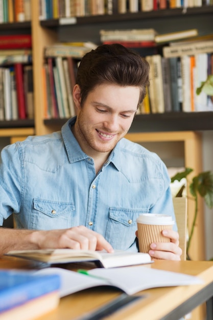 concetto di persone, conoscenza, istruzione e scuola - felice studente leggendo un libro e bevendo caffè in biblioteca