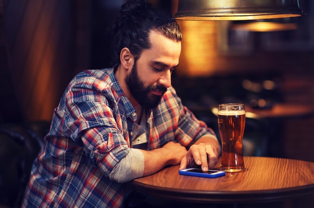 concetto di persone e tecnologia - uomo felice con smartphone che beve birra e legge un messaggio al bar o al pub