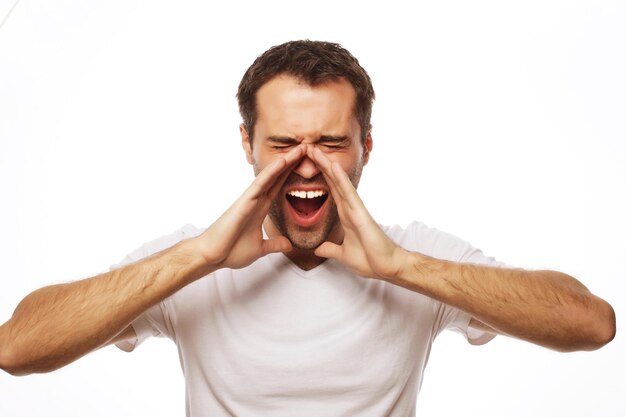 Concetto di persone, emozioni e stile di vita - bell'uomo in maglietta bianca che grida mentre guarda la fotocamera e in piedi su sfondo bianco