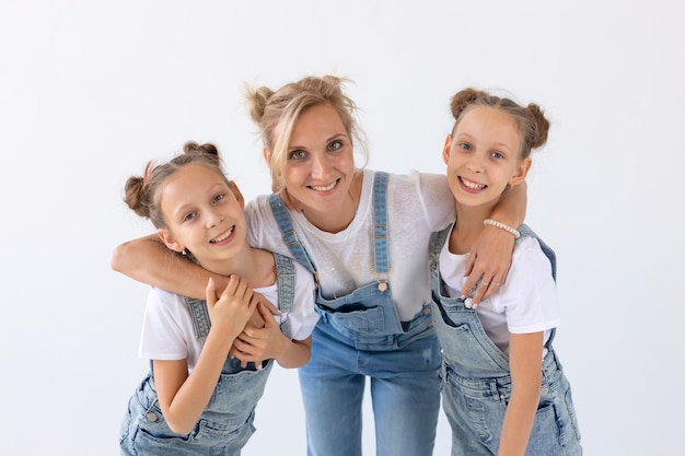 Concetto di persone, famiglia e bambini - ritratto di una madre adorabile che abbraccia le sue figlie gemelle su superficie bianca.