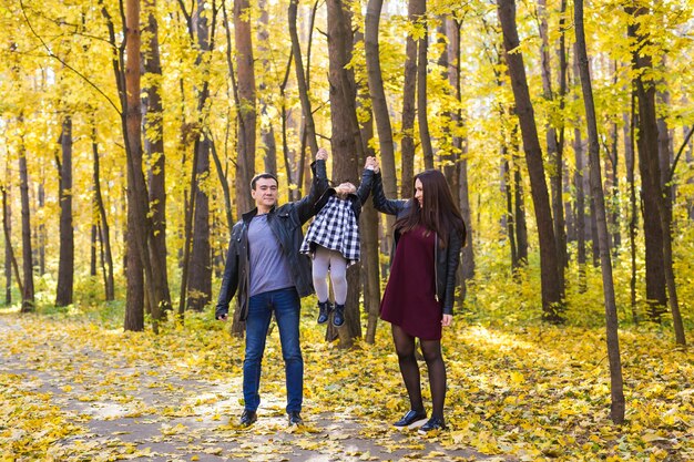 Concetto di persone, famiglia e tempo libero - famiglia felice con la figlia che cammina nella sosta di autunno