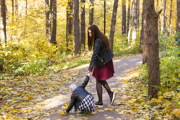 Concetto di persone, famiglia e tempo libero - giovane madre che cammina con sua figlia nel parco autunnale.