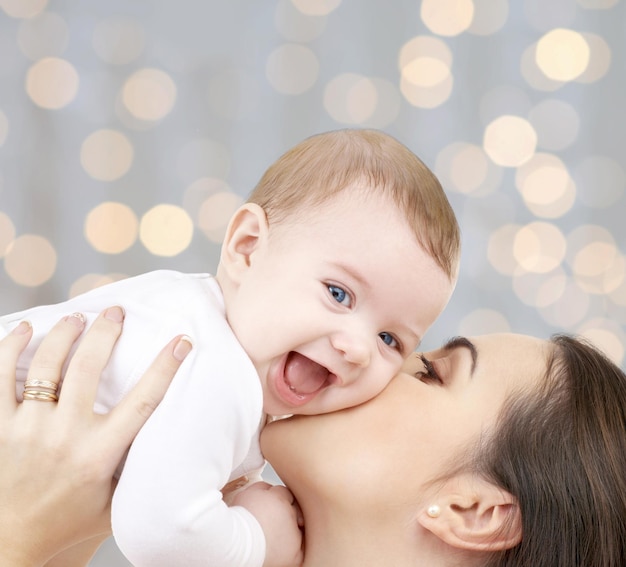 concetto di persone, famiglia, maternità e bambini - madre felice che abbraccia il bambino adorabile su sfondo di luci natalizie