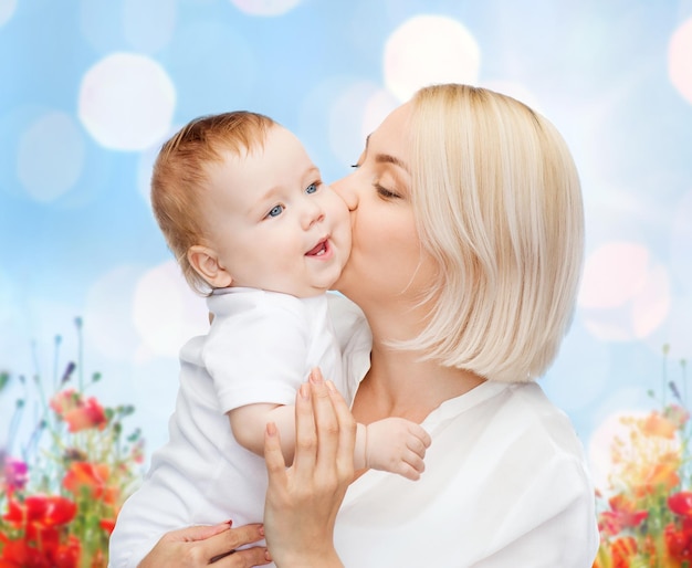 concetto di persone, famiglia, maternità e bambini - madre felice che abbraccia un bambino adorabile su luci blu e sfondo di campo di papaveri