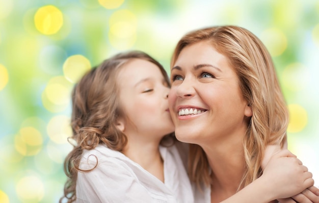 concetto di persone, felicità, amore, famiglia e maternità - figlia felice che abbraccia e bacia sua madre su sfondo di luci verdi