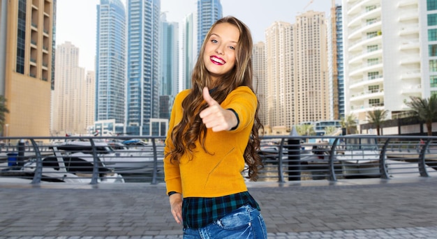 concetto di persone, gesti, viaggi, turismo e moda - giovane donna felice o ragazza adolescente in abiti casual che mostra i pollici in su sullo sfondo della strada della città di dubai