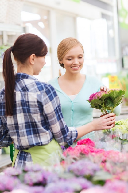 concetto di persone, giardinaggio, shopping, vendita e consumismo - giardiniere felice che aiuta la donna a scegliere i fiori in serra