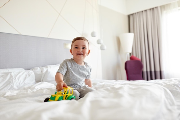 concetto di persone, infanzia e mattina - ragazzino felice con macchinina a casa o sul letto dell'hotel