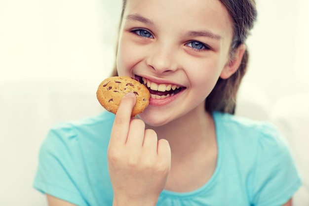 concetto di persone, infanzia felice, cibo, dolci e prodotti da forno - bambina sorridente che mangia biscotto o biscotto