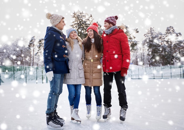 concetto di persone, inverno, amicizia, sport e tempo libero - amici felici che pattinano sul ghiaccio e si abbracciano sulla pista di pattinaggio all'aperto