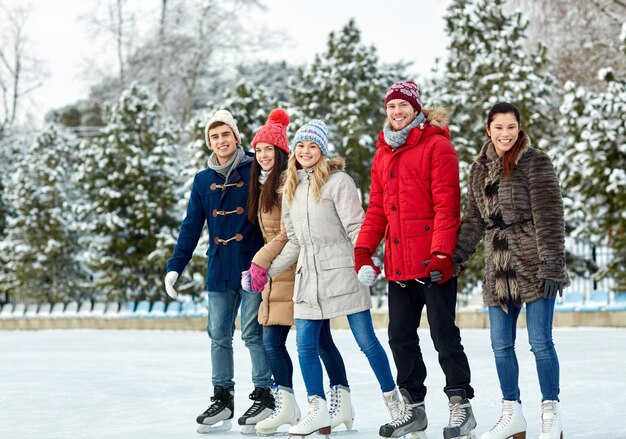 concetto di persone, inverno, amicizia, sport e tempo libero - amici felici che pattinano sul ghiaccio e si tengono per mano sulla pista di pattinaggio all'aperto