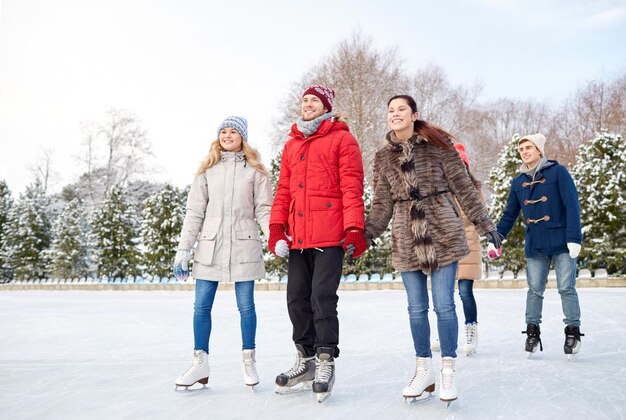 concetto di persone, inverno, amicizia, sport e tempo libero - amici felici che pattinano sul ghiaccio sulla pista di pattinaggio all'aperto