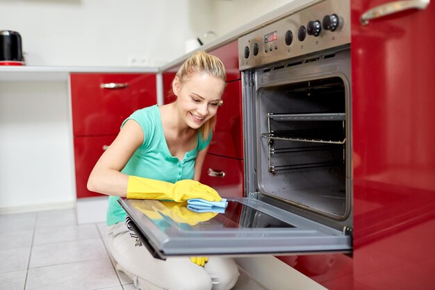 concetto di persone, lavori domestici e pulizie - donna felice che pulisce il fornello nella cucina di casa