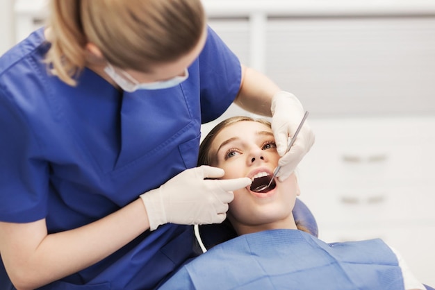 concetto di persone, medicina, stomatologia e assistenza sanitaria - dentista femminile felice con specchio che controlla i denti della ragazza del paziente all'ufficio della clinica dentale