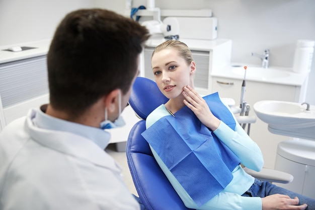 concetto di persone, medicina, stomatologia e assistenza sanitaria - paziente donna che parla con un dentista maschio e si lamenta di mal di denti presso l'ufficio della clinica dentale