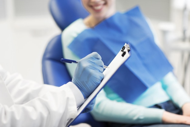 concetto di persone, medicina, stomatologia e assistenza sanitaria - primo piano del dentista con appunti e donna paziente felice presso l'ufficio della clinica odontoiatrica