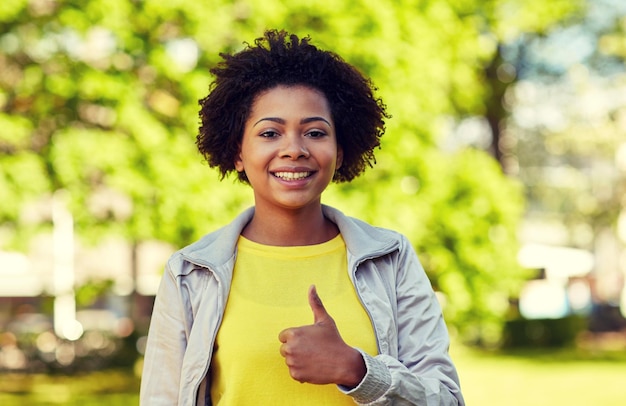 concetto di persone, razza, etnia e gesto - giovane donna afroamericana felice che mostra i pollici in su nel parco estivo