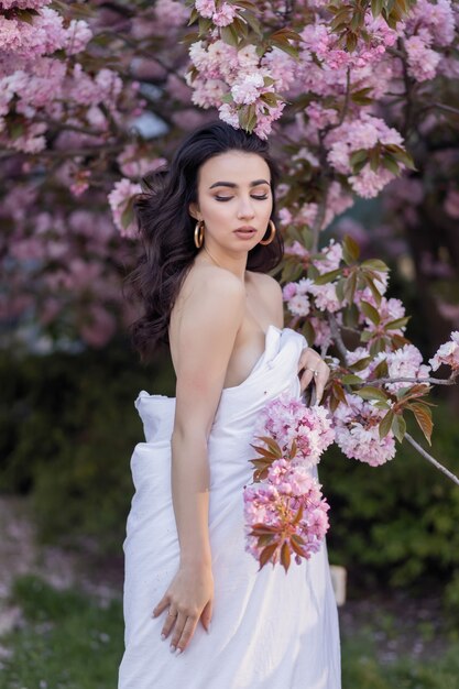 Concetto di persone, riposo, comfort e svago - Giovane donna per le strade serali avvolta in una coperta. Bella ragazza nel parco e un albero in fiore sakura