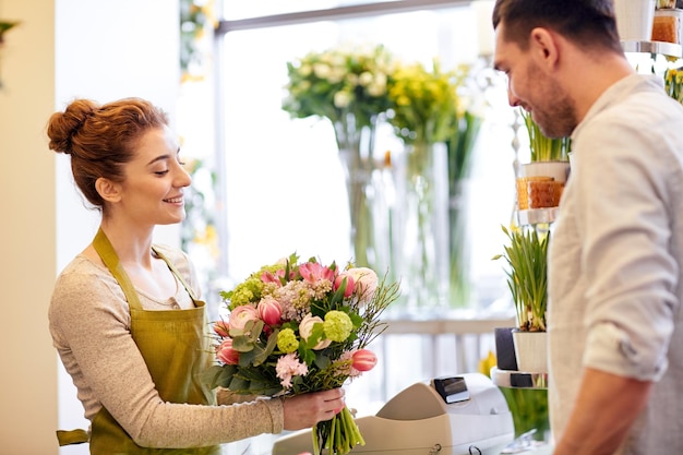 concetto di persone, shopping, vendita, floristica e consumismo - felice fiorista donna sorridente che fa bouquet per e uomo o cliente al negozio di fiori