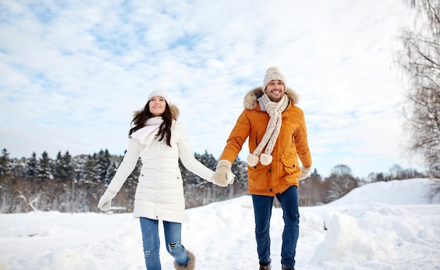 concetto di persone, stagione, amore e tempo libero - coppia felice che corre nella neve invernale