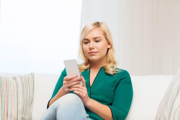 concetto di persone, tecnologia, comunicazione e tempo libero - felice giovane donna seduta sul divano con smartphone a casa