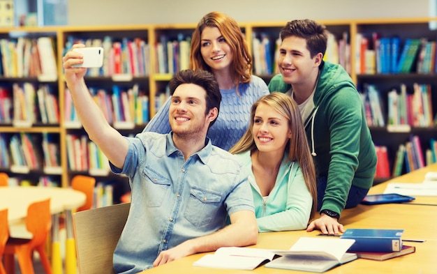 concetto di persone, tecnologia, istruzione e scuola - studenti o amici felici con smartphone che prendono selfie in biblioteca