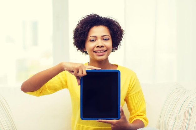 concetto di persone, tecnologia, pubblicità e tempo libero - felice giovane donna afroamericana seduta sul divano e che mostra lo schermo vuoto nero del computer tablet pc a casa