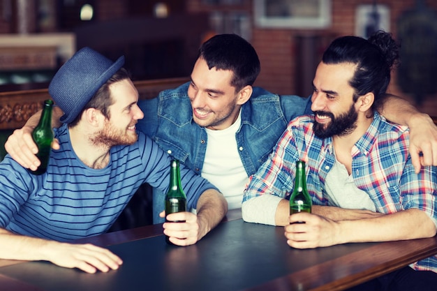 concetto di persone, tempo libero, amicizia e addio al celibato - amici maschi felici che bevono birra in bottiglia e parlano al bar o al pub