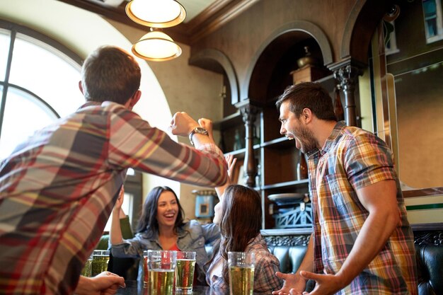 concetto di persone, tempo libero, amicizia e celebrazione - amici felici con birra che celebrano la vittoria al bar o al pub