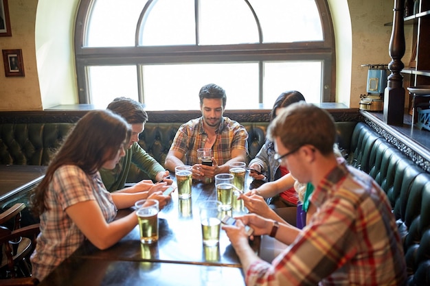 concetto di persone, tempo libero, amicizia e comunicazione - amici con smartphone che bevono birra e mandano SMS al bar o al pub