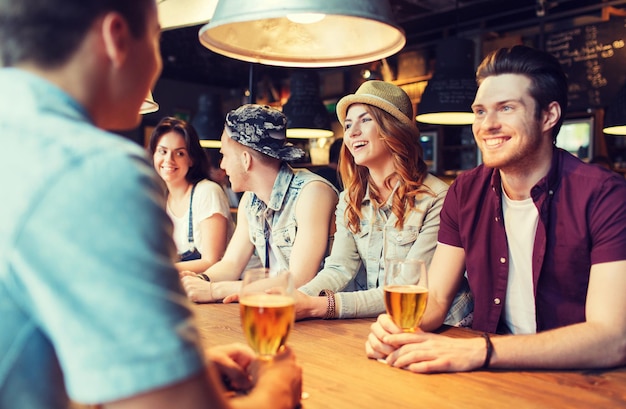 concetto di persone, tempo libero, amicizia e comunicazione - gruppo di amici sorridenti felici che bevono birra e parlano al bar o al pub