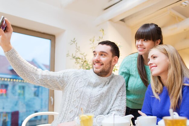 concetto di persone, tempo libero, amicizia e tecnologia - gruppo di amici felici con smartphone che prendono selfie e bevono tè al bar